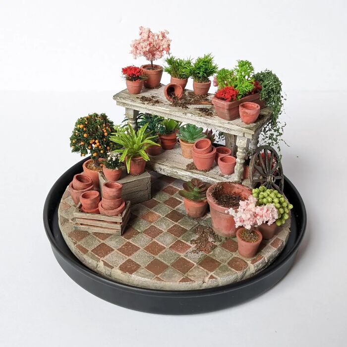 Miniature garden scene by Tamar Cohen with tiny terracotta pots and lush green plants on a round tiled base.