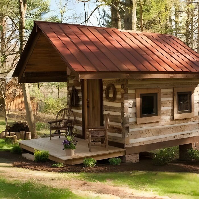 Small rustic wooden house with red metal roof and porch chair, showcasing beautifully crafted woodworking projects outdoors.