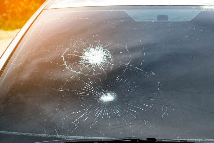 Car windshield with two large impact cracks under sunlight, symbolizing damage and conflict in relationships guys slept married woman why.