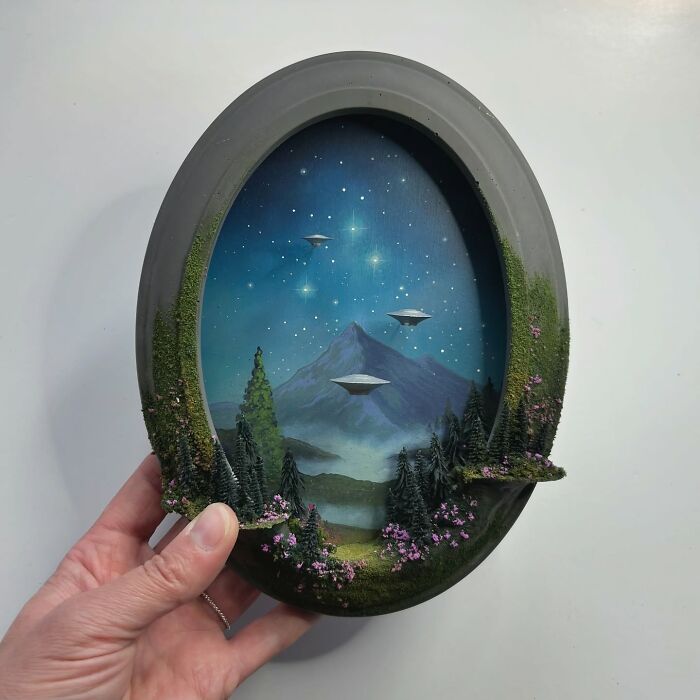 Hand holding an alien-themed diorama featuring UFOs and a mysterious starry mountain landscape.