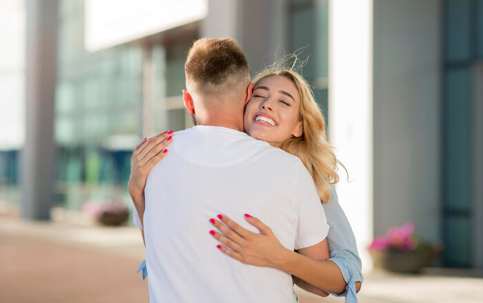 Woman smiling while hugging a man outside a modern building, showing dating dynamics.