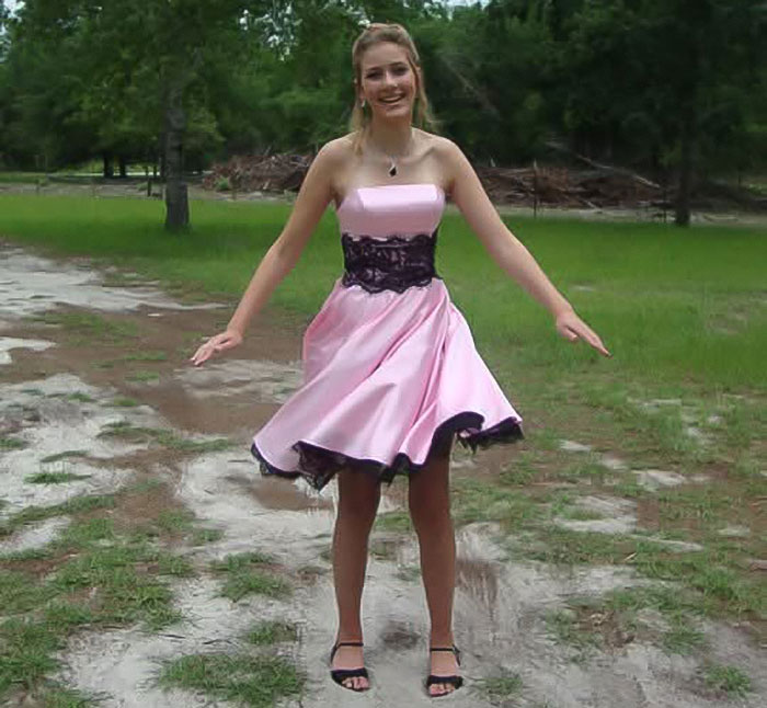 Tall cisgender woman in a pink dress standing outdoors on a dirt path with grass and trees. Tall cisgender woman in a pink dress standing outdoors on a dirt path with grass and trees.