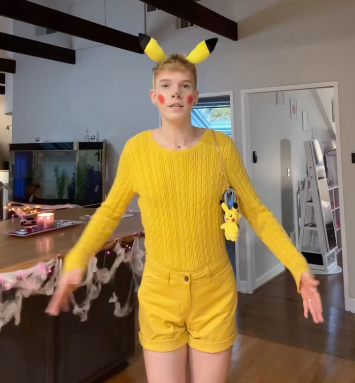 Person dressed in yellow outfit with Pikachu ears and plush, standing in a decorated room. Person dressed in yellow outfit with Pikachu ears and plush, standing in a decorated room.