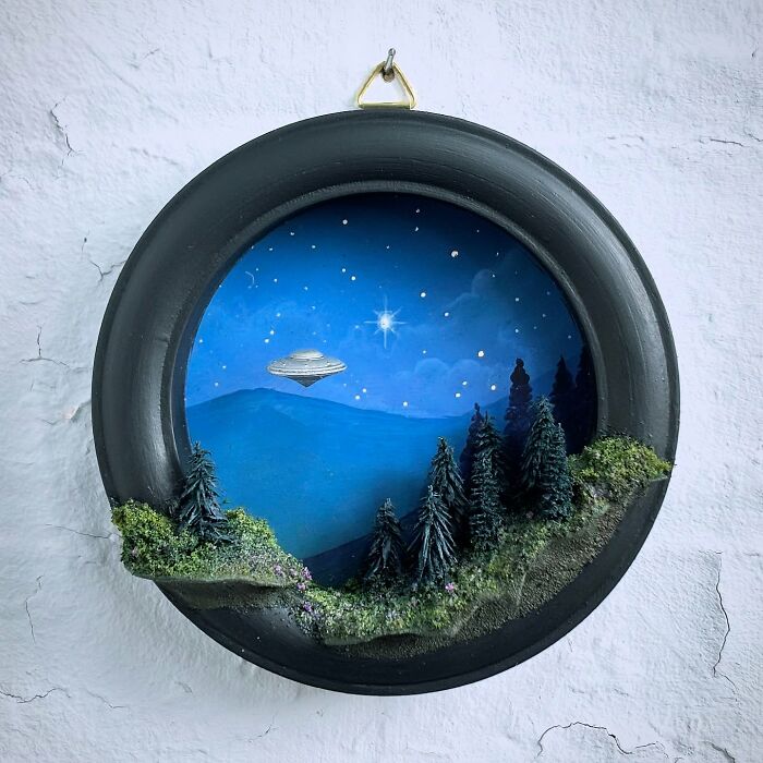 Circular diorama featuring an alien UFO in a starry night sky over a forested landscape.