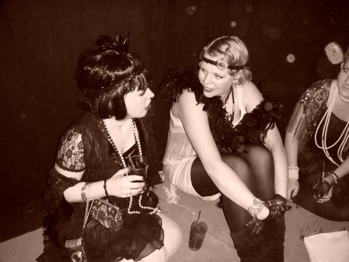 Three women dressed in vintage 1920s style outfits with flapper dresses and accessories at a social event. Three women dressed in vintage 1920s style outfits with flapper dresses and accessories at a social event.