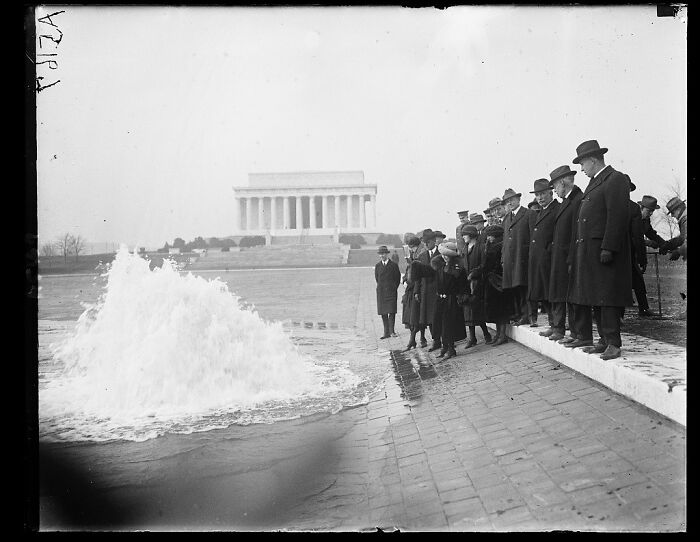 Group of men and women in early 1900s attire observing a fountain with Lincoln Memorial in the background, rare photographs restored.