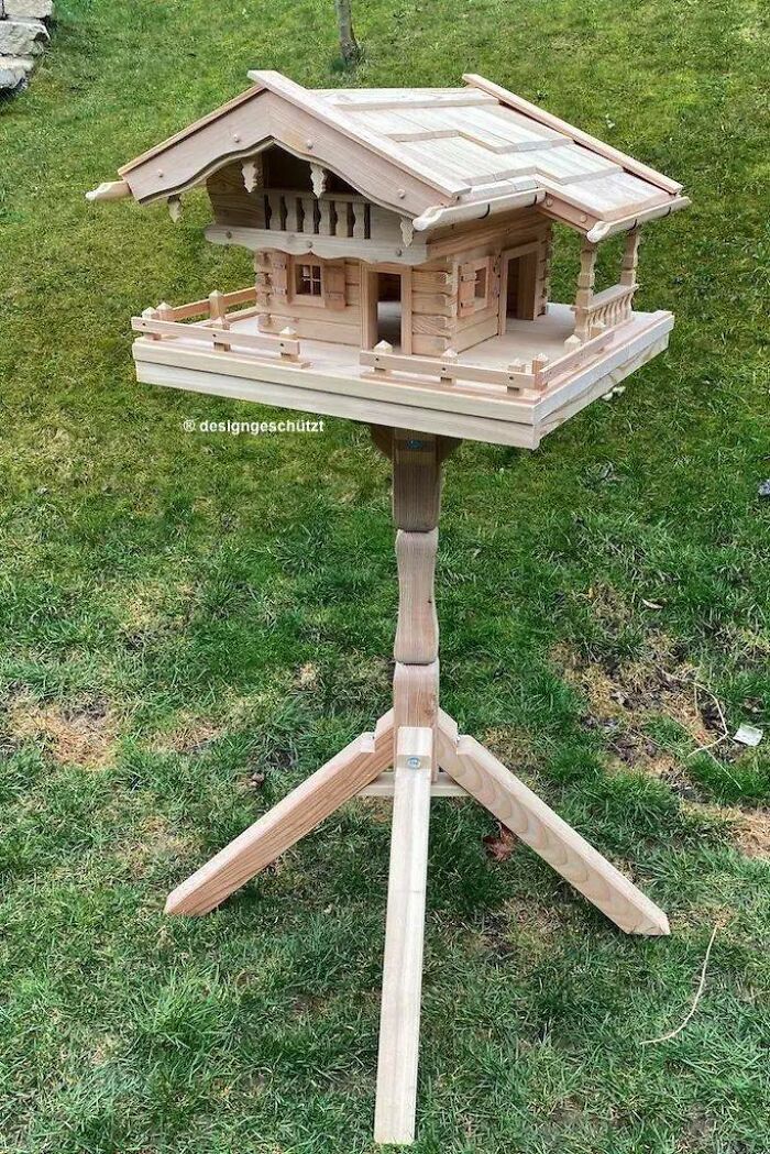Intricately crafted wooden birdhouse resembling a cabin, mounted on a tripod stand, showcasing impressive woodworking skills.