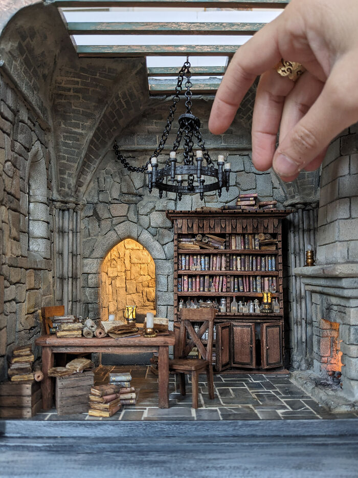 Hand interacting with Tamar Cohen's intricate miniature library, showcasing tiny books and a chandelier.