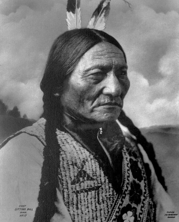 Portrait of Native American elder with traditional attire and feathers, illustrating real lives of Native Americans a century ago.
