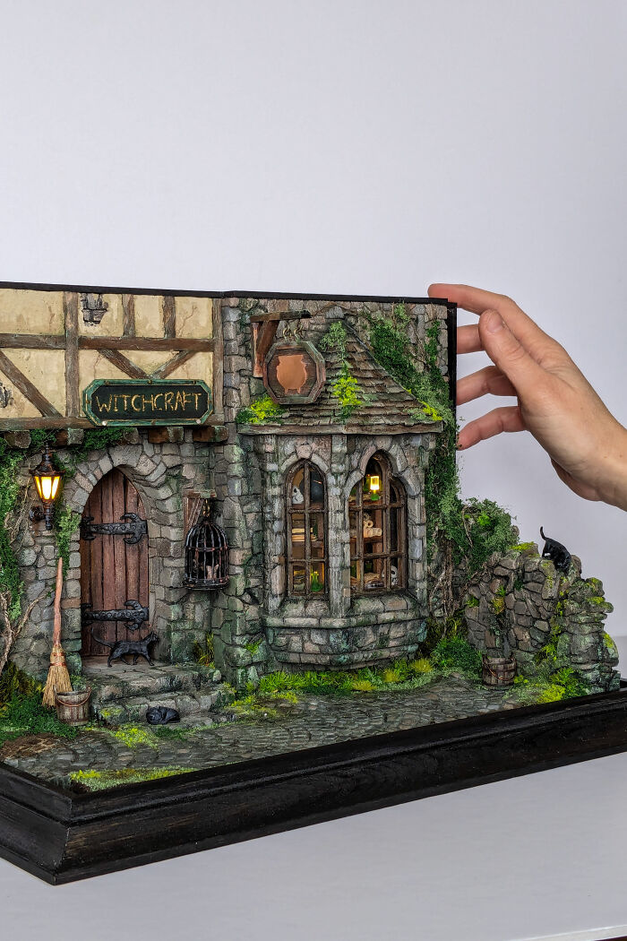 Miniature witchcraft-themed house by Tamar Cohen, featuring detailed stonework and greenery, held by a person's hand.