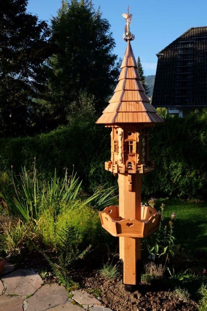 Intricately crafted wooden birdhouse with detailed design standing in a garden, showcasing impressive woodworking projects.