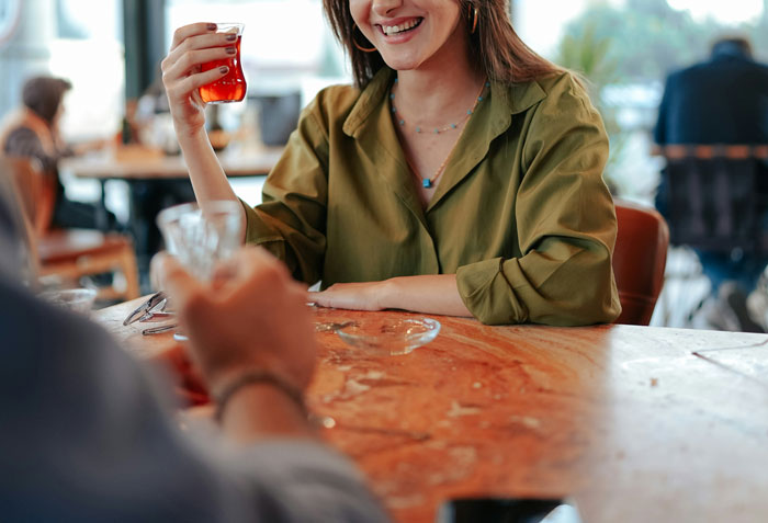 Woman in green shirt smiling over drinks at a table, depicting love and proposal theme. Woman in green shirt smiling over drinks at a table, depicting love and proposal theme.
