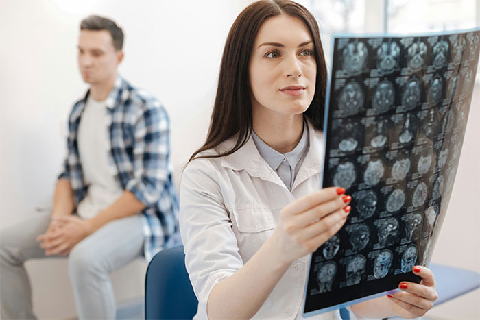 Doctor examines brain scan while a concerned man sits in the background, related to anger incident. Doctor examines brain scan while a concerned man sits in the background, related to anger incident.