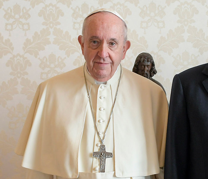 Pope Francis in a white robe, standing indoors with a serene expression, capturing mixed reactions. Pope Francis in a white robe, standing indoors with a serene expression, capturing mixed reactions.