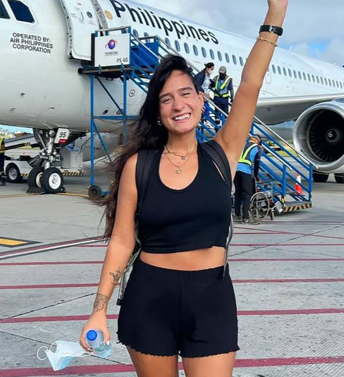 Smiling woman in black outfit stands in front of airplane, arm raised, before mysterious illness travel incident. Smiling woman in black outfit stands in front of airplane, arm raised, before mysterious illness travel incident.