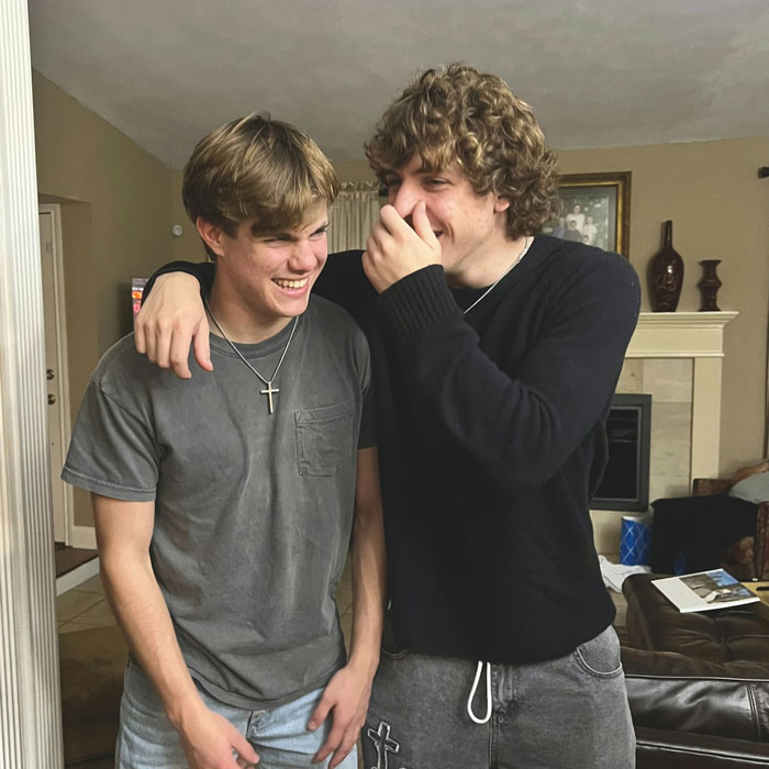 Two young men laughing indoors, one with his arm around the other in a casual setting, reacting to a prank. Two young men laughing indoors, one with his arm around the other in a casual setting, reacting to a prank.