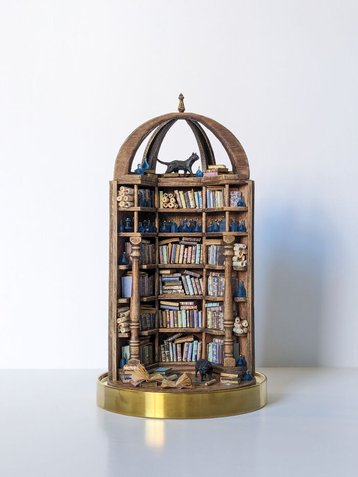 Miniature bookshelf by Tamar Cohen, featuring tiny books and scrolls, topped with a small animal figure.