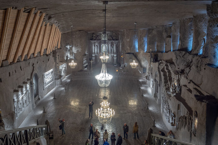 A vast underground city chamber with chandeliers, carved walls, and visitors exploring the eerie space.