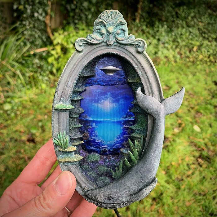 Alien-themed diorama by Caroline Dewison, featuring a UFO and ocean scene in a decorative oval frame with marine elements.