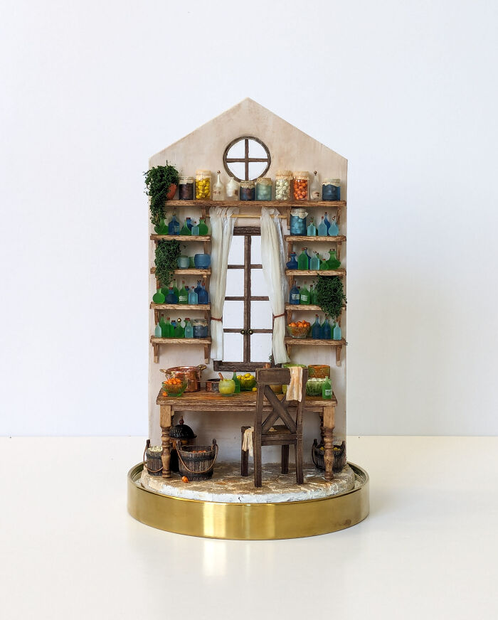 Miniature kitchen scene by Tamar Cohen featuring shelves with jars, a wooden table, and a chair, all in intricate detail.