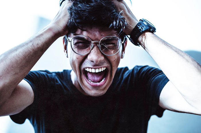 Man in distress wearing glasses and a black shirt, holding head with hands, reacting to a prank. Man in distress wearing glasses and a black shirt, holding head with hands, reacting to a prank.
