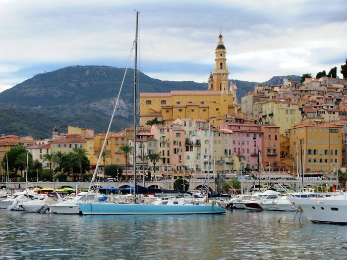 Colorful coastal cityscape with pastel buildings and boats, resembling a real-life painting.