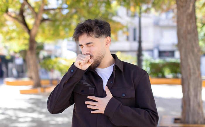 A man in a park, covering his mouth with a hand.