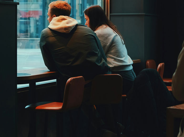 A couple sitting at a cafe window, discussing a family prank situation. A couple sitting at a cafe window, discussing a family prank situation.