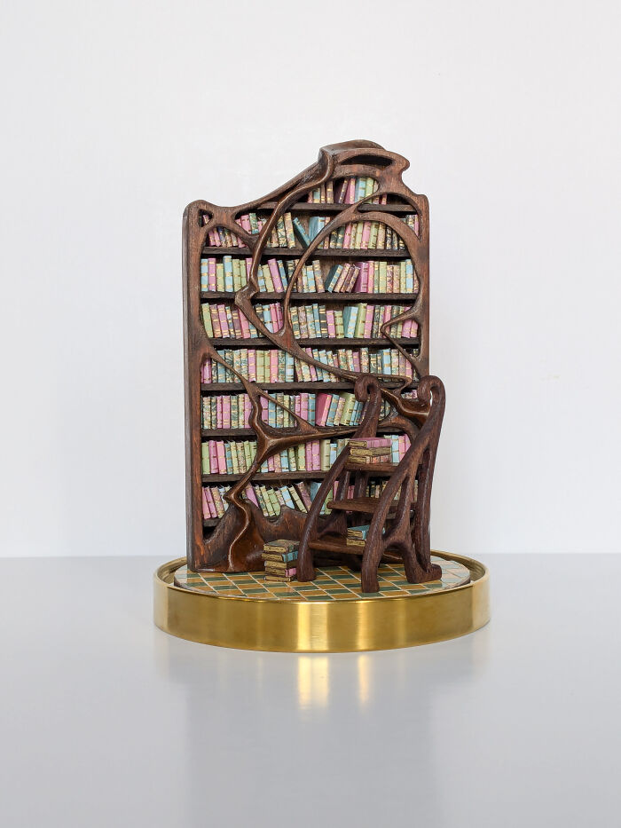 Miniature library sculpture by Tamar Cohen featuring intricate wooden shelves filled with colorful books and a small ladder.