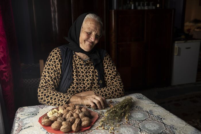Elderly woman in patterned attire, sitting by a table with walnuts, illustrating the vulnerability of aging women.