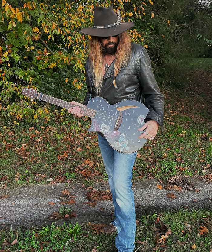 Man in a leather jacket and hat holding a decorated guitar, representing Billy Ray Cyrus' romance news. Man in a leather jacket and hat holding a decorated guitar, representing Billy Ray Cyrus' romance news.