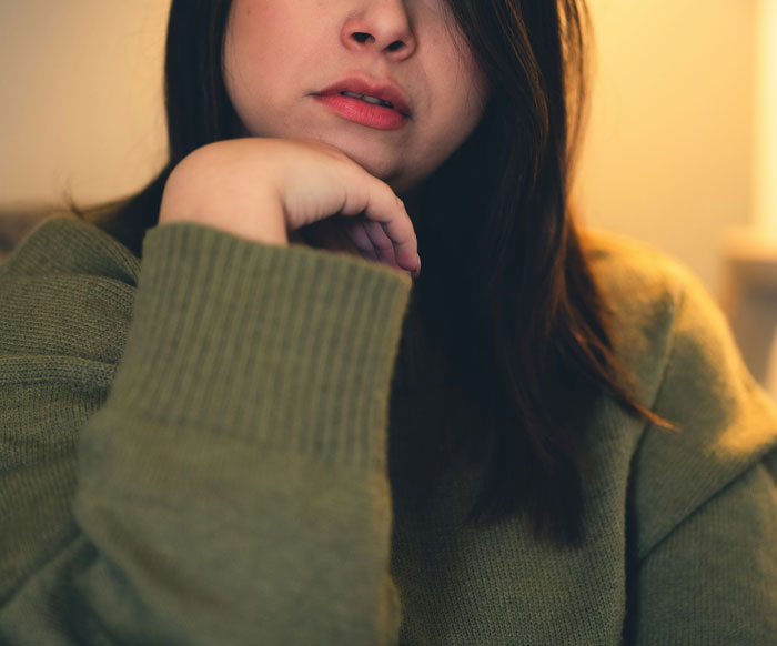 Woman in green sweater, slightly leaning on her hand with lips closed, expressing pensive mood related to cheating revelation. Woman in green sweater, slightly leaning on her hand with lips closed, expressing pensive mood related to cheating revelation.