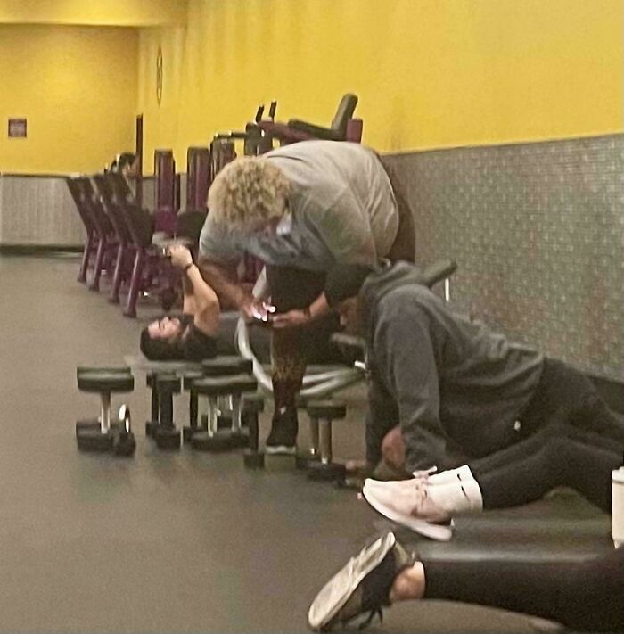 Person blocking gym equipment cluelessly, using phone, illustrating lack of self-awareness.