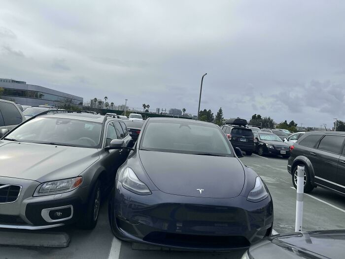 Crowded parking lot, showcasing a parked Tesla with no self-awareness in tight space.