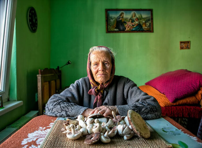 Elderly woman in a scarf at a table with mushrooms, depicting vulnerability of aging women.