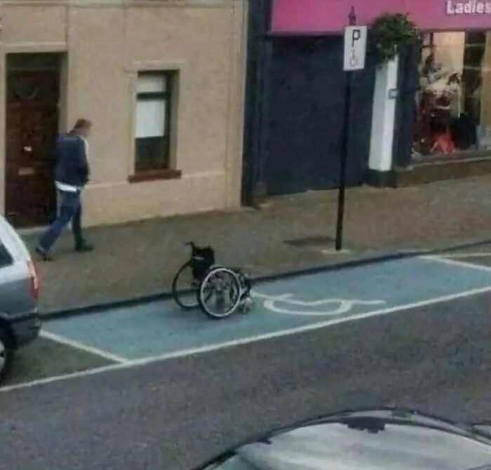 Wheelchair in a parking spot on the street, with a person walking by, illustrating a random cursed scenario. Wheelchair in a parking spot on the street, with a person walking by, illustrating a random cursed scenario.