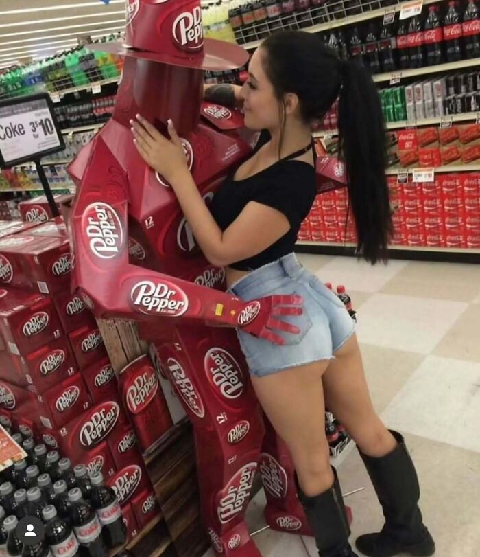 Woman posing with a humanoid figure made of Dr Pepper boxes in a grocery store aisle; random cursed image concept.