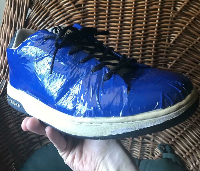 Failed repair attempt on a sneaker, covered in blue duct tape, held in hand.