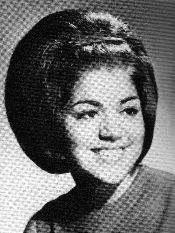 Retro woman with an enormous vintage hairstyle, smiling in a black and white photo.