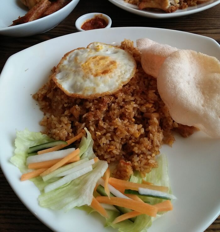 A plate of Nasi Goreng, a top dish from different countries, with a fried egg, crackers, and vegetable garnish.