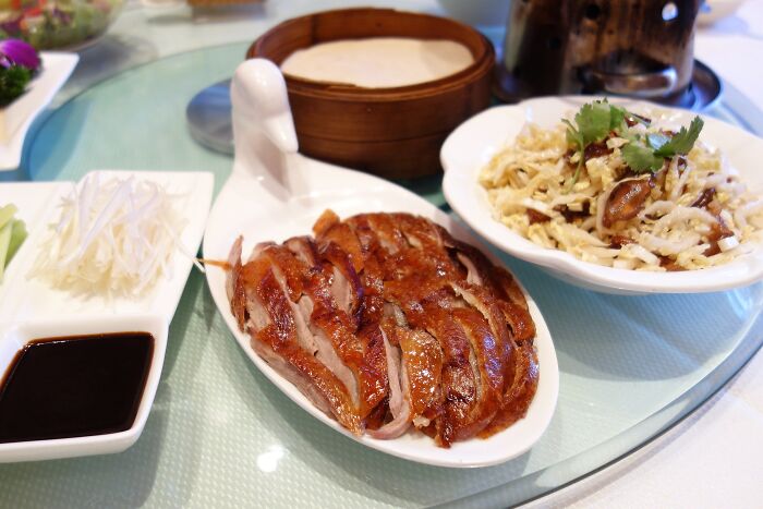 Sliced Peking duck with hoisin sauce and pancakes, a top dish from different countries, elegantly presented on a table.