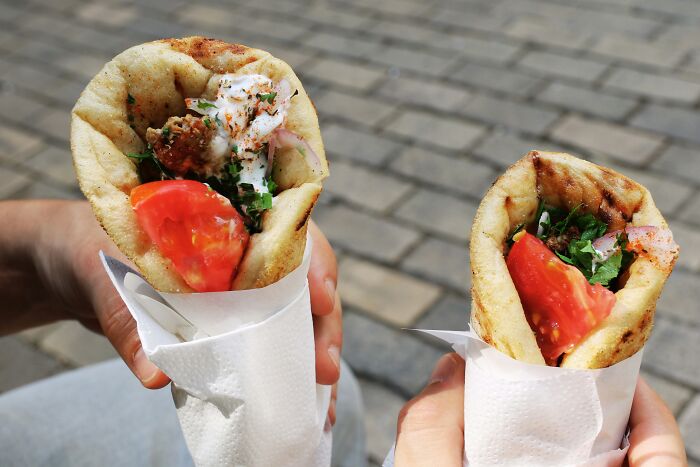 Two hands holding pita wraps with fresh vegetables and sauce, showcasing a top dish from different countries.
