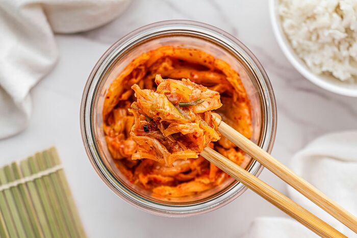 Chopsticks lifting kimchi from a glass jar, showcasing a top dish from different countries.