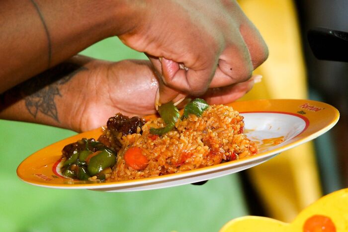 Close-up of hands serving vibrant rice dish on a colorful plate, showcasing top dish from different countries.