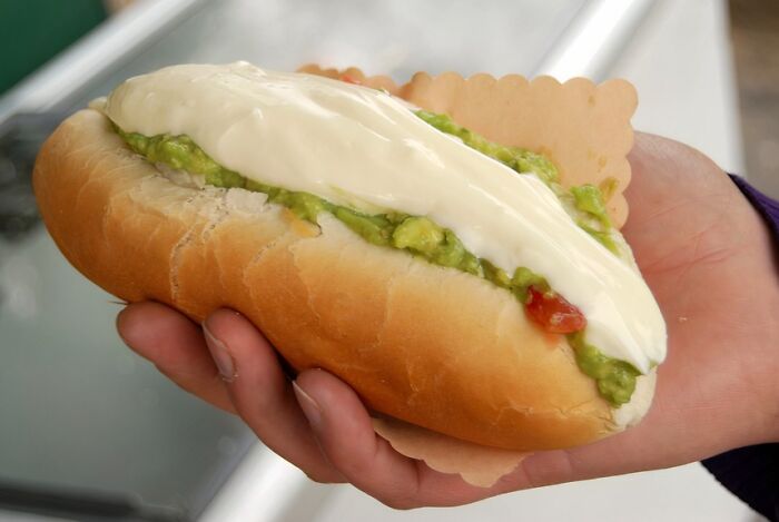 Hand holding a traditional Chilean hot dog loaded with toppings, showcasing a different country's top dish.