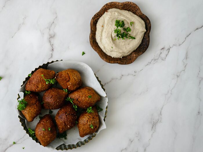 Plate of kibbeh garnished with parsley, served with a bowl of tahini sauce.