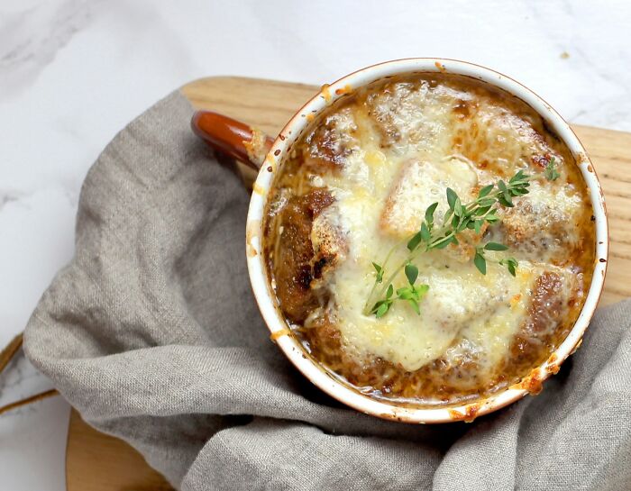 A classic top dish of French onion soup with melted cheese and herbs in a ceramic bowl.