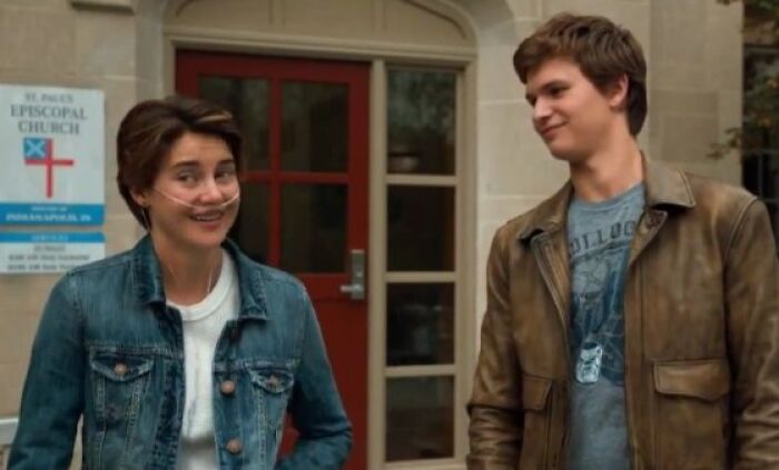 A young woman with a nasal cannula smiling at a young man in a leather jacket, outside a church.