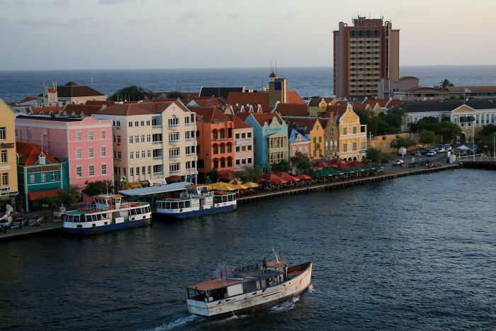 Colorful city buildings by the waterfront with a boat on the river, resembling a real-life painting.