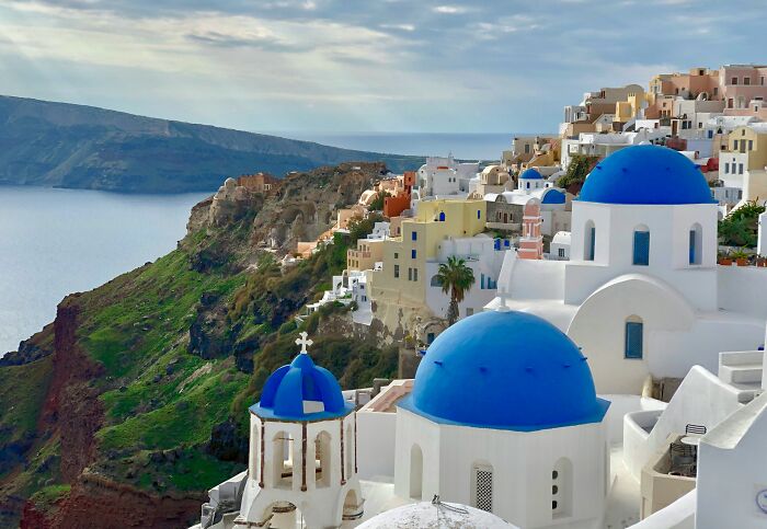 Colorful cityscape of blue-domed buildings on a cliff, resembling a real-life painting.